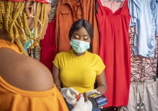 A closeup of an African female with latex gloves and a facemask paying with a credit card at a shop